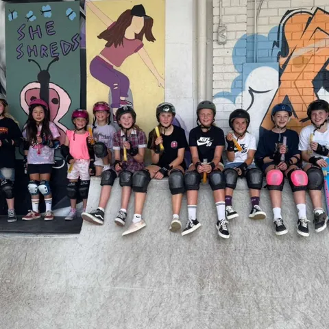 Skaters sitting in a row in front of a mural