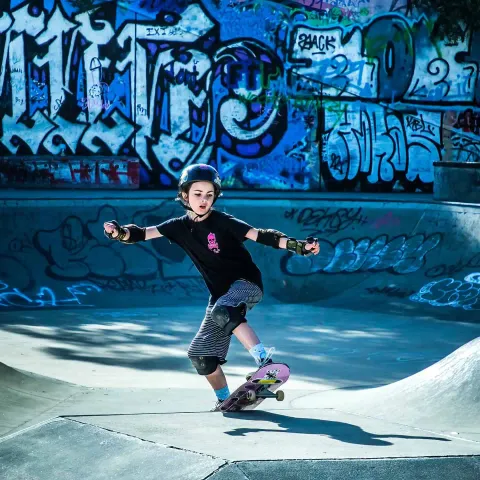 Skater riding a bowl in front of a graffiti wall
